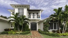 a white house with lots of palm trees in front of it and a brick walkway leading to the door