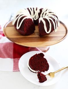 a red velvet bundt cake with white icing on a wooden platter next to a fork