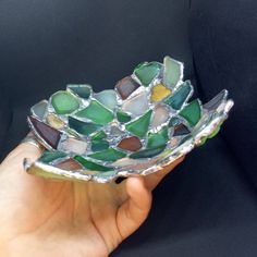 a hand holding a glass bowl with green and brown designs on it's sides