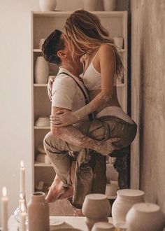 a man and woman kissing in front of a table with white vases on it