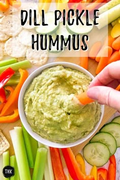 a person dipping dip into a bowl filled with hummus surrounded by veggies and crackers