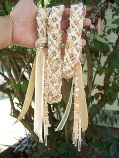 a hand is holding three bracelets with tassels on them in front of a tree