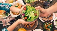 several people are holding their hands over a table full of plates and bowls of food