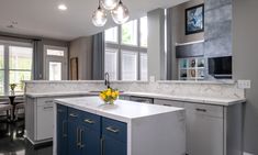 a kitchen with white and blue cabinets, marble counter tops and an island in the middle