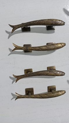 three antique brass drawer pulls on a white surface, one has a fish tail design