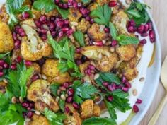 a white plate topped with cauliflower and pomegranate covered in greens