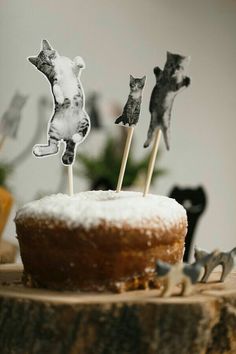 a cake topped with three cats on top of a wooden table next to cupcakes