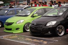 several cars are parked in a parking lot with people standing around the cars and looking at them