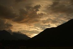 the sun is setting in front of some mountains with clouds above it and grass below