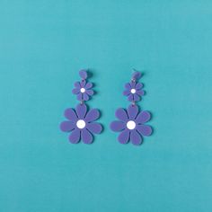 two purple flowers are attached to the back of some earring's on a blue background