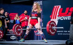 a woman holding a barbell during a crossfit competition with other people watching