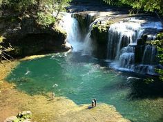 two people are standing in the water near a waterfall and another person is walking up to it