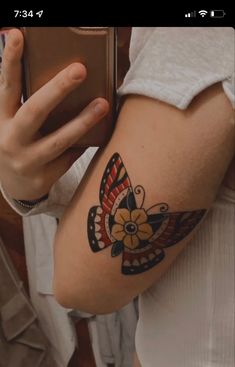 a woman with a butterfly tattoo on her arm holding a cell phone and taking a selfie