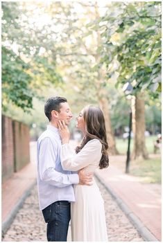 a man and woman standing next to each other on a brick walkway in front of trees