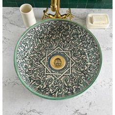 a bathroom sink with an intricate design on the bowl and gold faucet above it