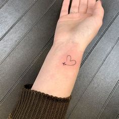 a woman's hand with a small heart tattoo on her left wrist and an arrow in the middle