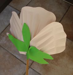 a paper flower with green leaves on it sitting on a tile floor next to a wall