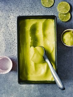 a pan filled with ice cream next to lime slices and spoons on a table