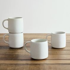 three white coffee mugs sitting on top of a wooden table next to each other