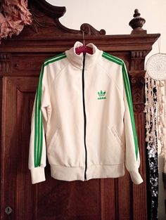 Stunning timeless Vintage Adidas track jacket with beautiful color way - ivory white with green iconic three stripes along the shoulders and sleeves, green Adidas Trefoil on the left breast. Black front zipper. Regular straight cut, raglan sleeves. Ribbed cuffs and waistband. Two side pockets. Unisex - can be worn by women or men. Simply stunning when combined casual with sneakers, jeans or track pants! ERA: 2000s BRAND: Adidas Original COLOR: Ivory white, green, black FABRIC: No fabric tag anym Vintage Adidas Track Jacket, Casual White Track Jacket With Side Stripes, White Track Jacket With Three Stripes, Retro White Track Jacket For Streetwear, White Long Sleeve Track Jacket With Three Stripes, White Three Stripes Long Sleeve Track Jacket, Retro Track Jacket With Three Stripes, Retro Long Sleeve Track Jacket With Three Stripes, Retro White Cotton Track Jacket