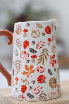 a ceramic pitcher with autumn leaves and acorns painted on the side, sitting on a wooden table