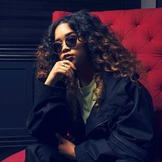 a woman sitting in a red chair with her hand on her chin and looking off to the side