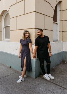 a man and woman standing next to each other on the sidewalk near a tall building