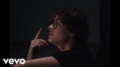 a young man with glasses pointing at something in the dark while looking to his left