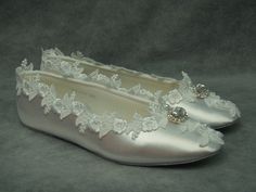 a pair of silver shoes with white lace and pearls on the bottom, sitting on a gray background