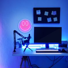 a desk with a computer on it and a neon sign above the monitor that says 90