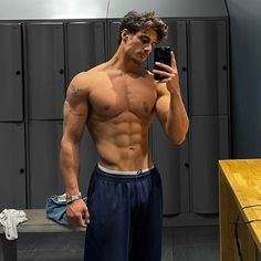 a shirtless man taking a selfie in front of lockers with his cell phone