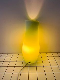 a yellow lamp sitting on top of a white tiled floor next to a light bulb