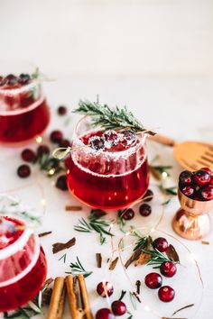 two glasses filled with cranberry shrub and cinnamon stick garnished with rosemary