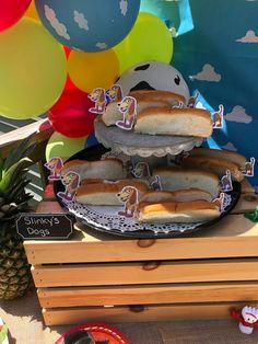 two hot dogs on buns sitting on top of a table with balloons in the background