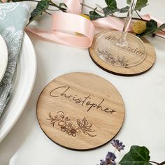 two personalized wooden coasters sitting on top of a table next to some flowers