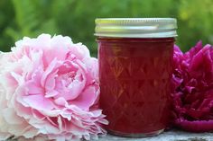 two pink flowers sitting next to a jar filled with jam on top of a wooden table