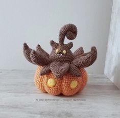 a crocheted stuffed animal sitting on top of a pumpkin with horns and eyes