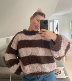 a woman taking a selfie with her cell phone in front of her, wearing a striped sweater