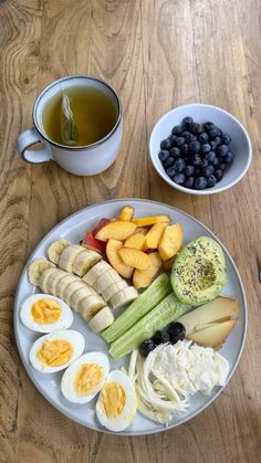 an assortment of fruits and vegetables on a plate next to a cup of green tea