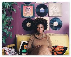 a woman sitting on top of a couch in front of record wall with vinyl records