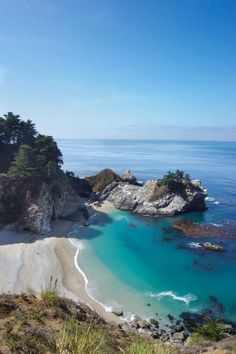 an ocean beach with clear blue water and trees on the shore, surrounded by rocky cliffs