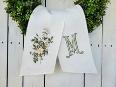 two white towels with embroidered monograms and flowers on them hanging from a door