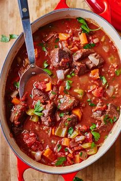 a pot filled with meat and vegetables on top of a wooden table next to a spoon