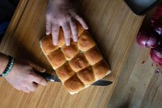 a person cutting up some bread on top of a wooden table next to onions and a knife