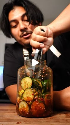 a man holding a knife over a jar filled with vegetables