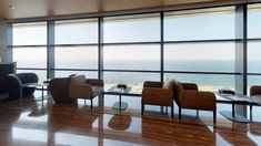 an empty room with chairs and tables overlooking the ocean in front of large glass windows