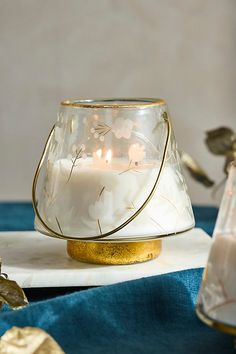 a glass candle holder sitting on top of a white marble slab with gold trimming