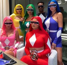 four women dressed in costumes posing for a photo with one woman wearing sunglasses and the other holding a cell phone