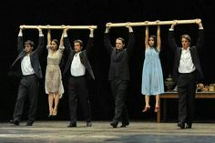 five people are standing on stage with their arms in the air and one man is holding two wooden bars above his head