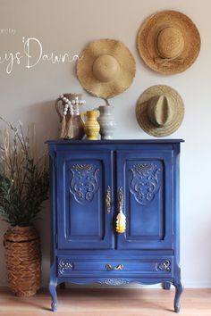 a blue cabinet with two hats on top of it and a plant in the corner